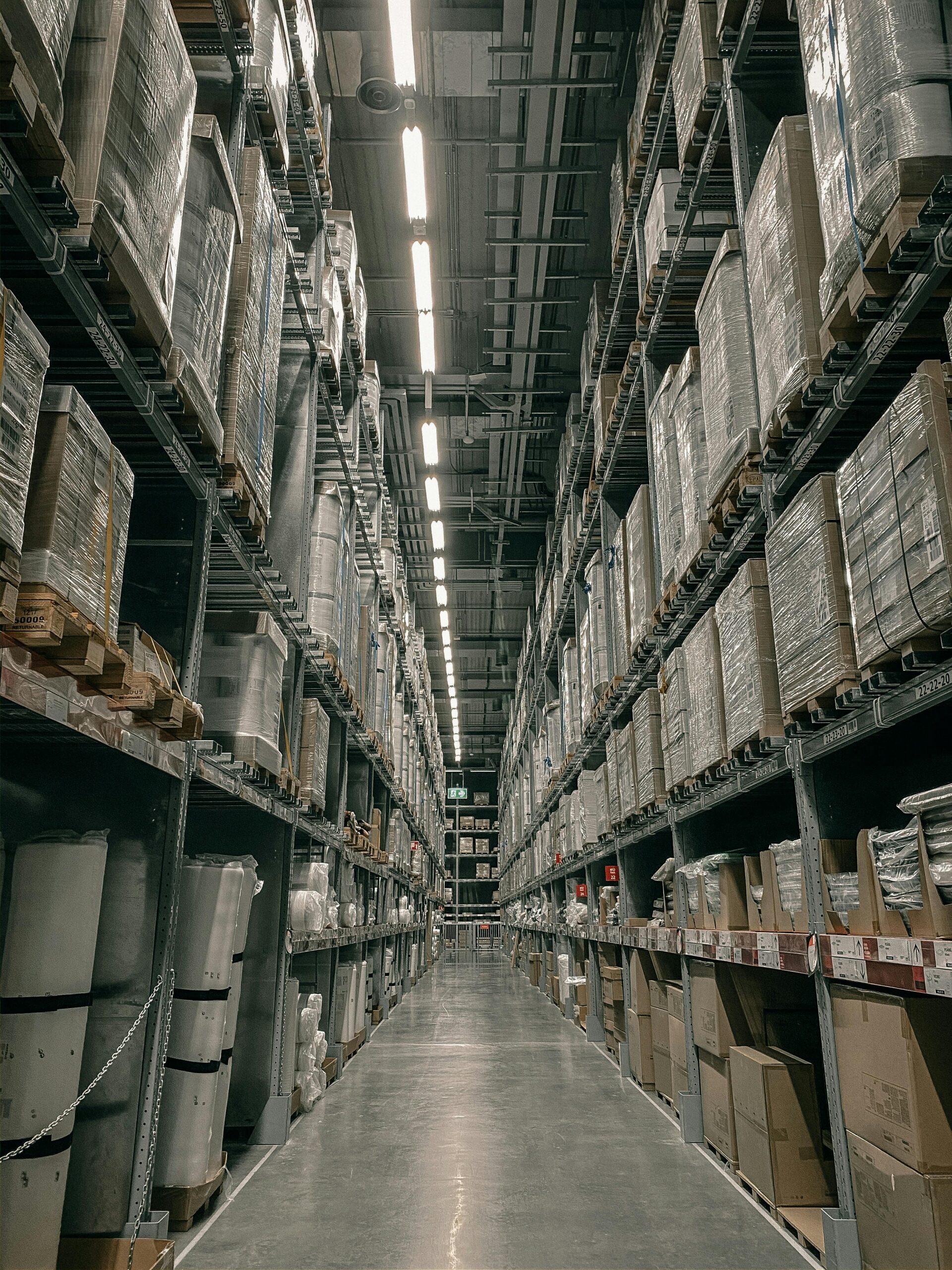 Home A long aisle in a modern warehouse with high shelving filled with boxes and supplies.